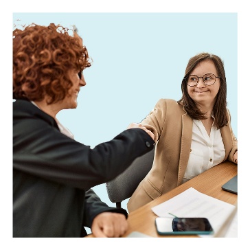 2 people beside each other at a desk shaking hands.